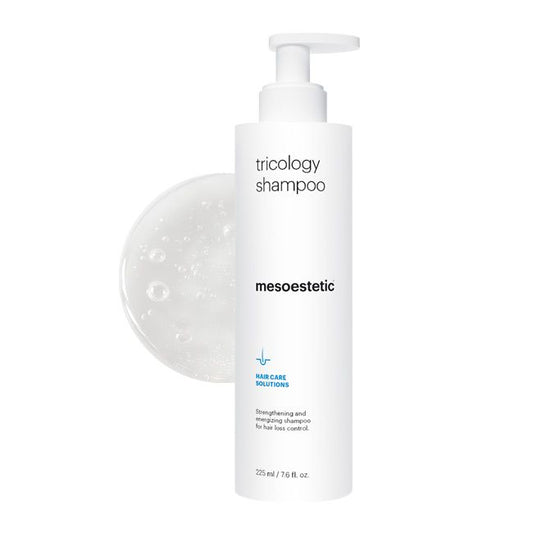A pump bottle of Mesoestetic Trichology Hair Loss Shampoo with bubbles forming around it, indicating the product is a liquid.
