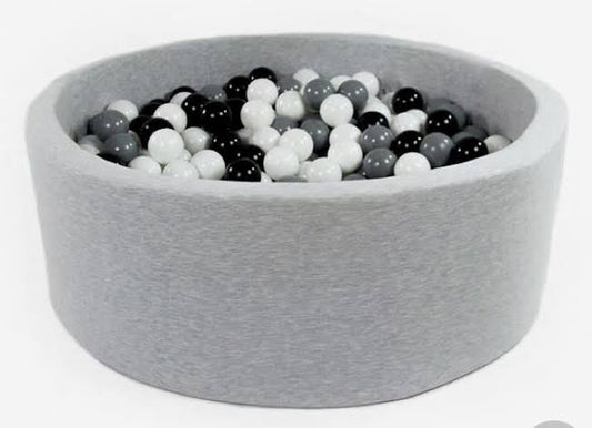 A round gray fabric ball pit filled with white and black plastic non-toxic balls.