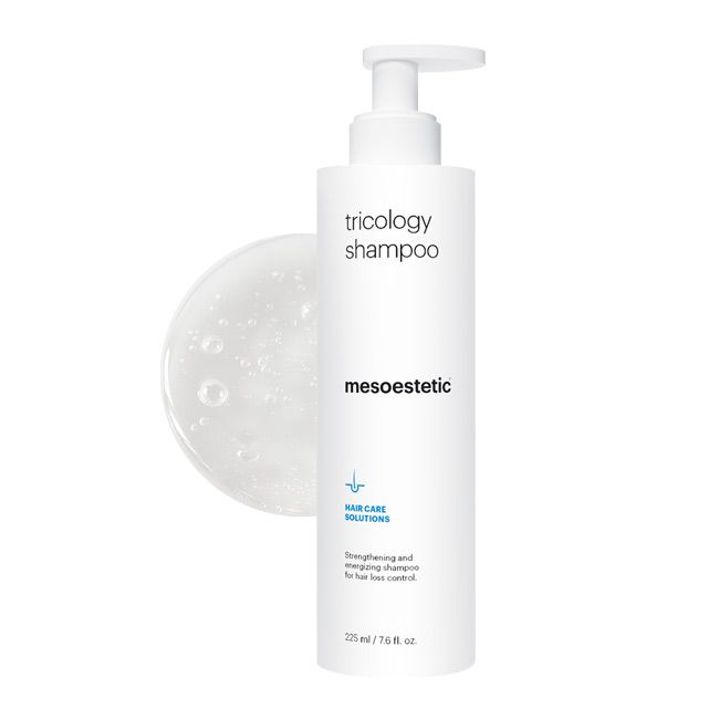 A pump bottle of Mesoestetic Trichology Hair Loss Shampoo with bubbles forming around it, indicating the product is a liquid.